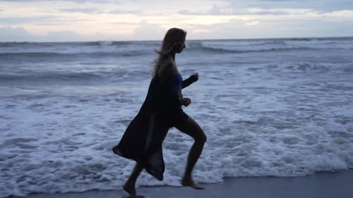 Junge Frau beim Fallen lustig und frei und springt barfuß am Strand bei Sonnenuntergang