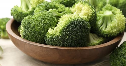 Fresh green broccoli in bowl on white table, closeup. Camera moving left