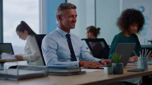 Joyful businessman waving hand during video call in bright modern office