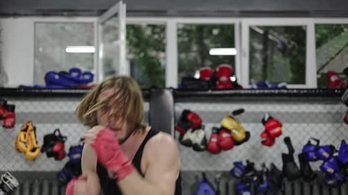 Concentrated Man Wearing Boxing Gloves and Training in Gym with Grey Walls