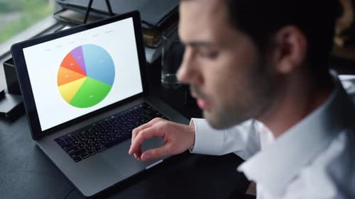 Serious Businessman Working on Laptop Computer at Home Office. Male Freelancer Pointing
