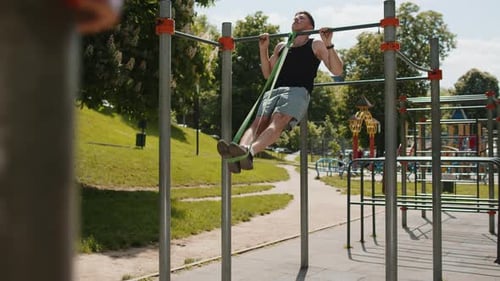 Athletic Man in Sportswear Doing Pullups Exercises on Horizontal Bar with Help of Elastic Expander