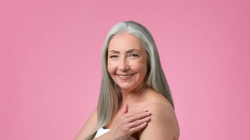 Senior Woman With Gray Hair Smiles and Poses Against a Pink Background in a Light Cheerful Setting