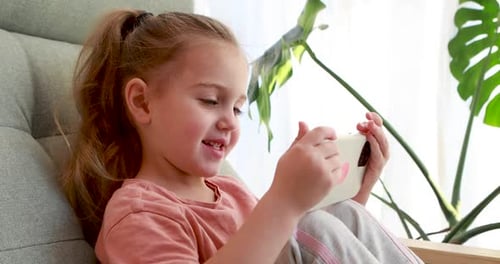 Cute Little Girl with Smartphone Sitting on Armchair Close Up