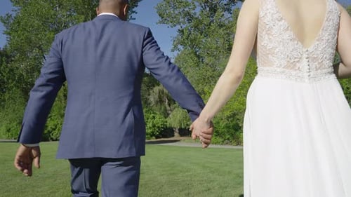 Groom and bride walking hand in hand on a farm on their wedding day. Slow motion.