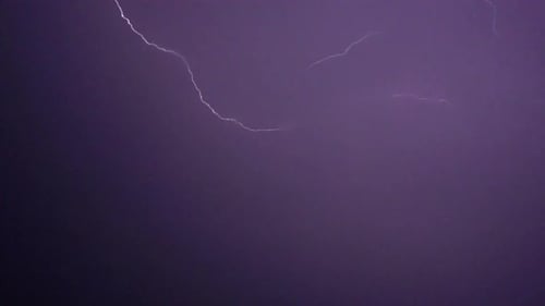 Flashes of lightning in the night sky among thunderclouds.