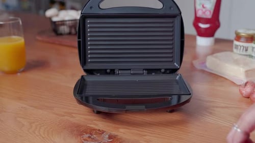 Female putting sliced lettuce tomato cheese panini sandwich on electric grill