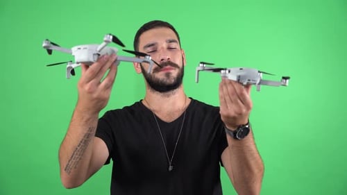 Young man inspects two drones on green screen 4K