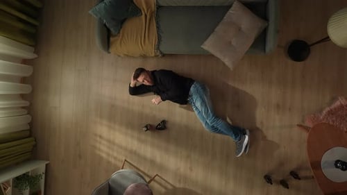 Top View of a Man Smoking a Cigarette Lying on the Living Room Floor Near an Ashtray and a Whiskey