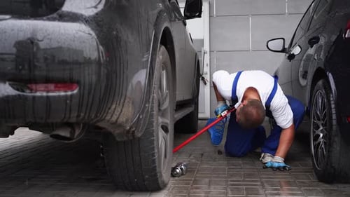Auto Mechanic in Uniform Uses Hydraulic Jack to Lift Car for Tire Change Professional Garage Worker