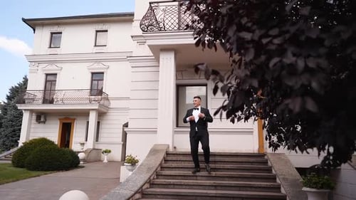 Herrischer Mann in schwarzem Anzug und Fliege geht die Marmortreppe hinunter aus seiner Luxusvilla Millionär