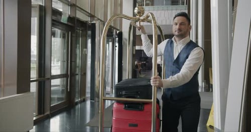 Dolly Shot of Helpful Bellman Pushing Trolley with Luggage Along Hotel Corridor