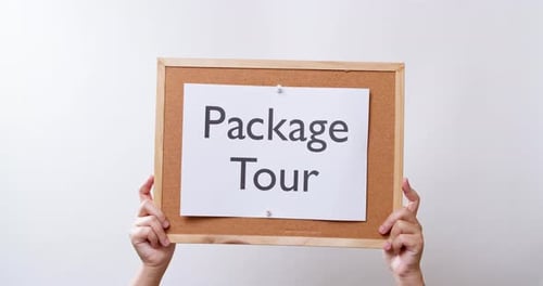 Woman's hand shows the paper on board with the word Package Tour in white studio background with cop