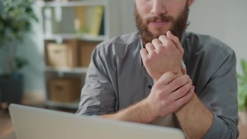 Man Rubs Sore Wrist While Working on Computer
