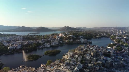 Golden hour aerial of Udaipur, India, showing lakes, dense white neighborhoods, islands, and