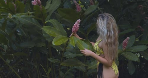 Chica de pelo rubio juega con una flor de chaconia en un sexy bikini de tanga