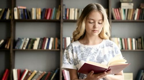 Attractive blonde teenage student reads in a library close up indoors