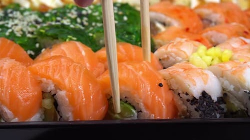 Hand hold chopsticks with sushi roll. Philadelphia roll in sushi set close up. Traditional Japanes