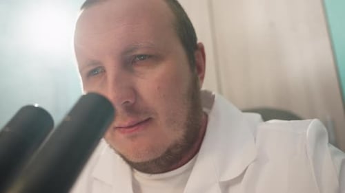 Man Examining Sample Through Microscope in Laboratory
