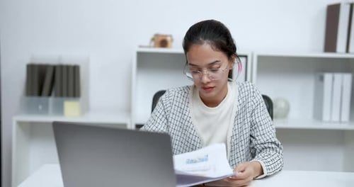 Woman Reviews Documents at Desk with Laptop