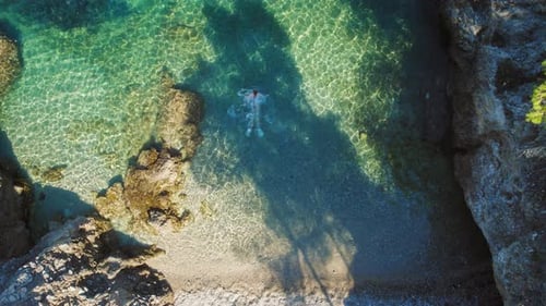 Swimmer floating in shallow turquoise waters near rocky beach in Kefalonia Greece