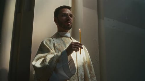 Young Priest Reciting Prayer Holding Burning Candle in Catholic Church
