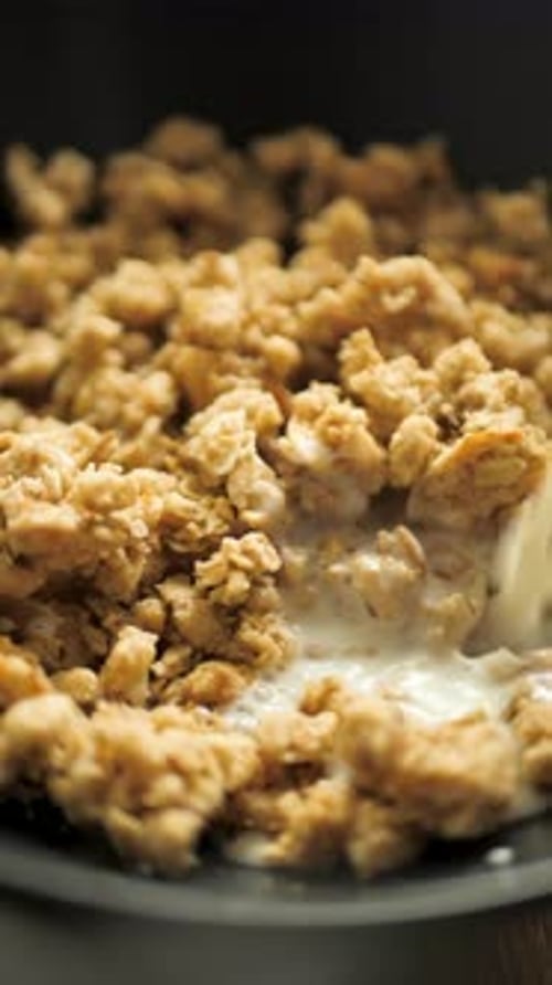 Vertical Orientation A Stream of Fresh Milk Pours Into Oat Granola in a Black Bowl Slow Motion
