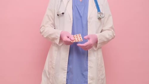 Woman doctor holding pills, studio pink background. Nurse in uniform with stethoscope on red studio