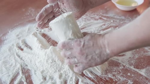 A cook in a bakery kitchen pours flour into a measuring cup.