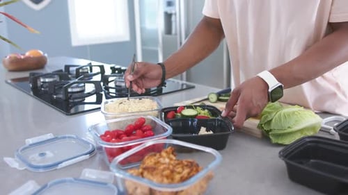 Homme afro-américain plaçant des récipients transparents, ramassant du riz dans des boîtes à repas noires au comptoir
