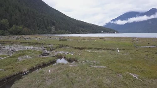 Low aerial flyover of grassy tidal flat toward ocean inlet with marina