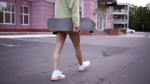 A Girl Walks in the Park with a Skateboard in Her Hands a Daily Hobby