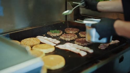 Burger patties, bacon, and buns on a grill