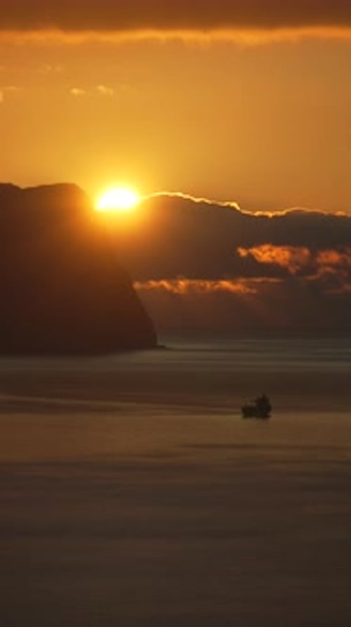 Sunset Sea Ship Golden Sun Setting Behind Dark Cliffs Over a Calm Ocean with a Silhouetted Boat in