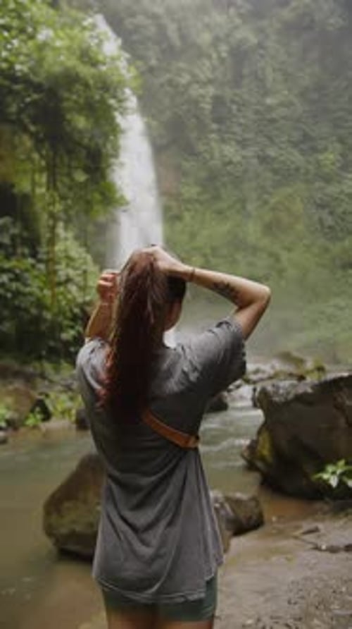 Girl Standing Back to the Camera Looking at a Waterfall in the Jungle Vertical
