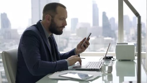 Young businessman working online using smartphone and laptop in modern office