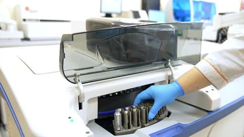 Medical laboratory assistant places a stand with a test tube into the machine.