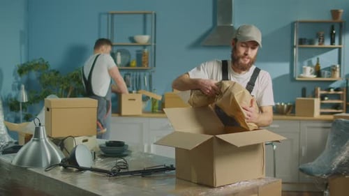 Workers of Moving Company With Uniforms Carefully Packing Things at Boxes