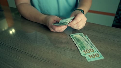 Person counting one hundred dollar bills on table