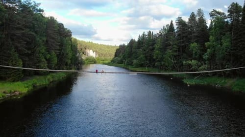 Tourists Relaxing on Rope Bridge Over Scenic River