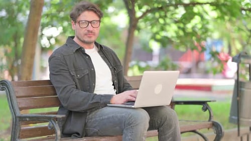 Man Working on Laptop Giving Thumbs Down in Park