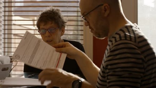 Elderly Woman Sorting Documents With Help From Adult Son At Home On Spring Afternoon Medium Shot