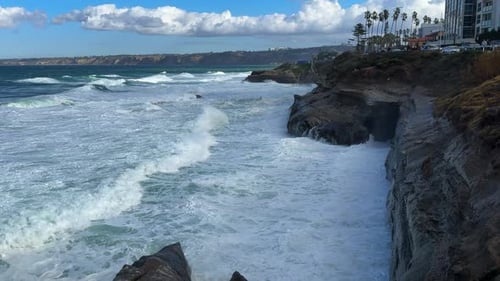 King tide at La Jolla Cove skyline view over waves crashing on cliffs.