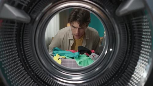View From Inside the Washing Machine Young Man Holding a Bottle of Fabric Softener and Washing