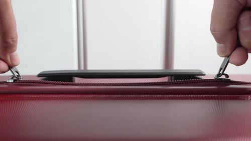 A close-up video shows hands pulling two zippers on a red suitcase.