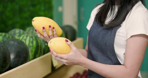 Close-up of hands holding and examining fresh yellow mangoes in a well-organized fruit shop,