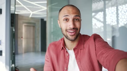 POV Smiling businessman talking on a video call using a phone in modern business office. Confident