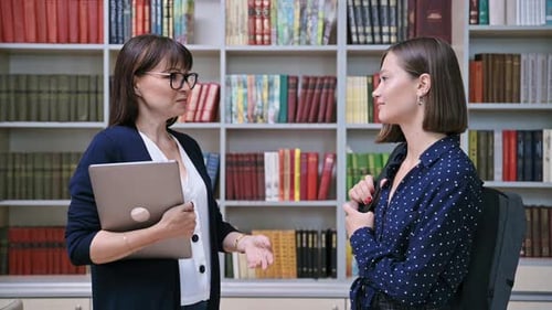 Woman Teacher Talking to Female Student Inside College Library