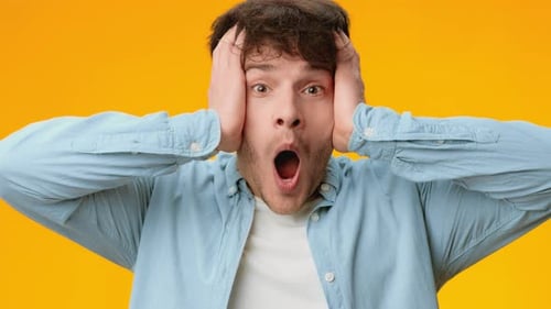 Shocked Young Man Hands to Face on Orange