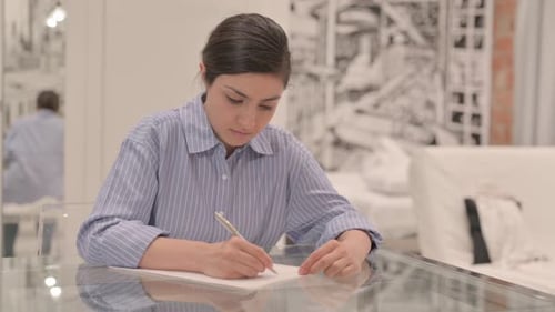 Young Adult Writing on Paper at Glass Table